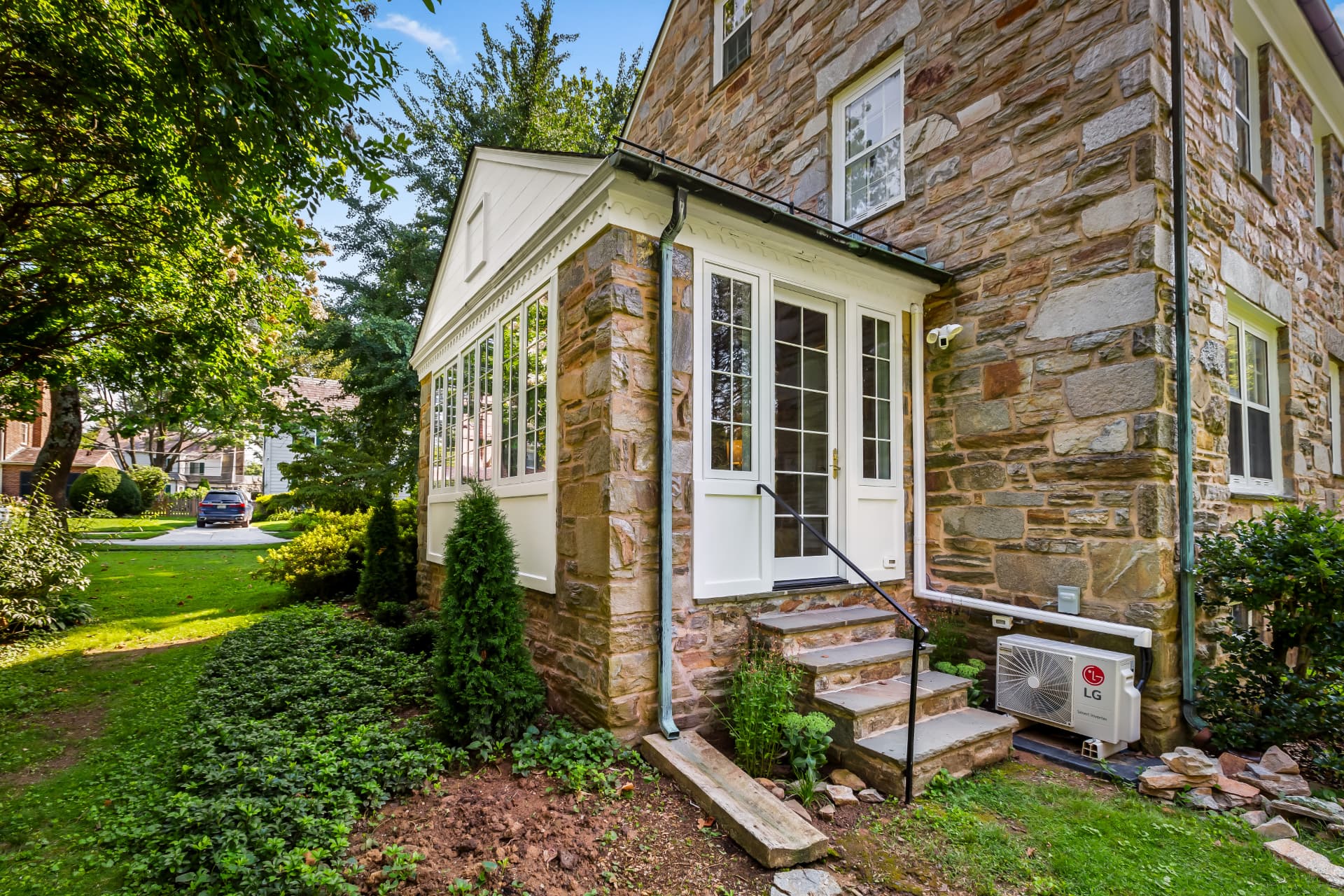 Scherr custom home addition with stone facade, white sunroom windows, and landscaped garden